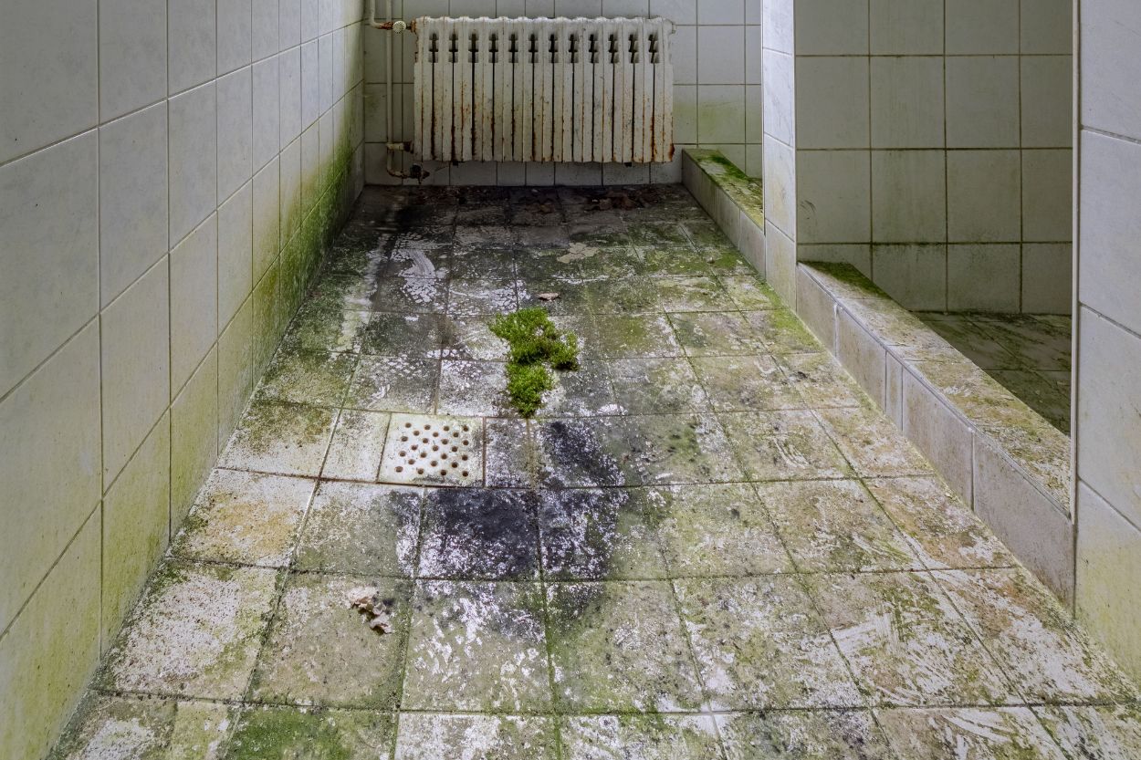 A dilapidated bathroom with a dirty floor and radiator, underscoring the demand for mold removal services in Austin, TX.
