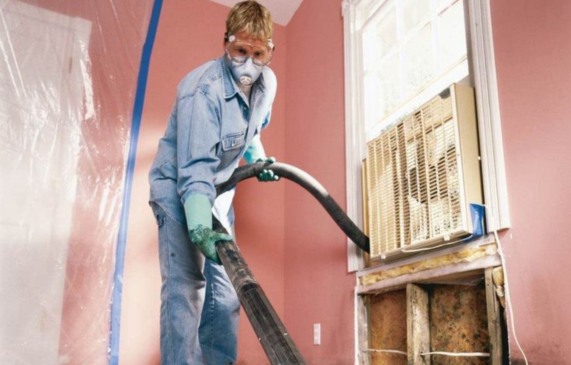 A man wearing a blue shirt and overalls cleans a room with a vacuum, representing a mold removal service in Austin, TX.