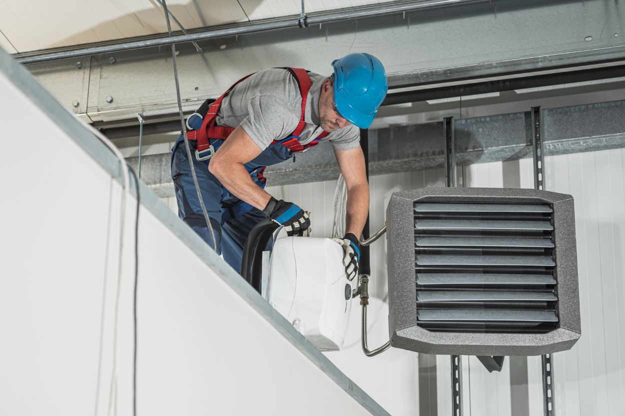 A man wearing a hard hat and safety vest is fixing an air conditioner for an HVAC mold removal service in Austin, TX.