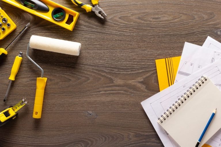 A variety of construction tools, including a hammer, screwdriver, and pliers, arranged on a wooden table surface.